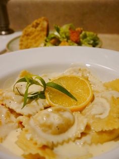 a white plate topped with pasta covered in sauce and garnished with lemon wedges