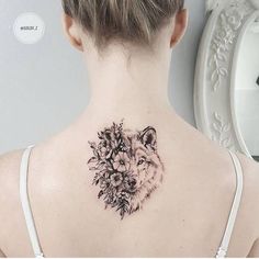 a woman's back neck with a wolf and flowers tattoo on her left shoulder