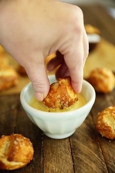 a person dipping something into a small white bowl filled with sauce on top of a wooden table