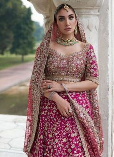 a woman in a red and gold bridal outfit standing next to a white pillar