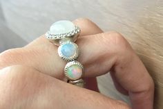 "A gorgeous shimmery round Cabochon Moonstone statement ring accented with a halo of white topaz complemented with 7 cabochon opals on the shank, handcrafted in sterling silver, makes this a unique engagement ring or great statement ring.(r-c-183) These are cabochon opals on the shank, which extreme care needs to be taken not to break the stones as they rank 6 on Mohs hardness scale meaning, they are a soft and fragile gemstones. Avoid immersing in water or washing the dishes with the ring on an White Jewelry With Halo Setting And Round Band, White Jewelry With Halo Setting, White Halo Setting Jewelry With Round Band, White Multi-stone Moonstone Ring Fine Jewelry, White Opal Ring With Accent Stones, Bohemian White Opal Ring, Adjustable Fit, White Rings With Gemstone Accents, White Round Multi-stone Jewelry, Opal Rings With Gemstone Accents