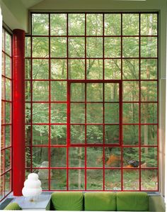 a green couch sitting in front of a window next to a red pillar and table