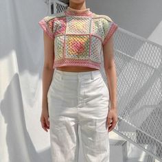 a woman wearing white pants and a crocheted top standing in front of a wall