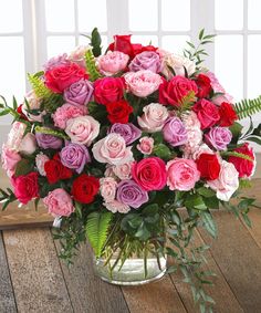 a vase filled with pink, red and purple flowers on top of a wooden table