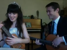 a man and woman are playing guitars in the living room while wearing tiaras