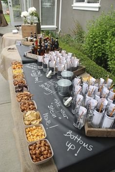 a long table topped with lots of food and drinks on top of a black cloth covered table