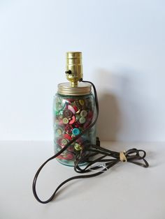 a glass jar filled with buttons sitting on top of a white table next to a cord