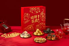 a red table topped with plates and cups filled with desserts next to a phone