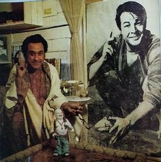 a man sitting at a table in front of a painting with a baby doll next to him