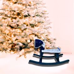 a wooden rocking horse in front of a christmas tree with snow on the top and bottom