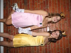 two girls dressed in costumes standing next to each other near a brick wall and holding hands