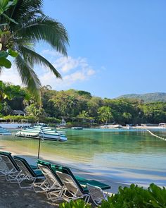 lounge chairs and umbrellas are lined up on the beach next to boats in the water