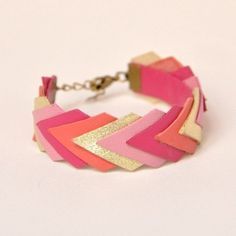 a pink and gold bracelet on a white surface with a chain hanging from the wrist