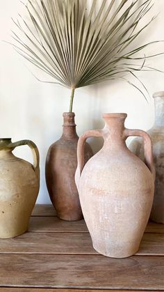 three vases are lined up on a wooden table with a palm tree in the background