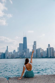 a woman sitting on the edge of a pier pointing at the city