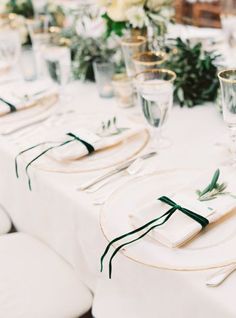 the table is set with white linens and green ribbon on each place setting, along with silverware