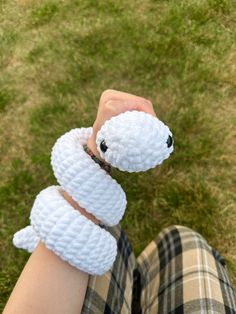 a person holding a white stuffed animal in their hand on the grass with green grass behind them