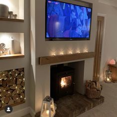 a television mounted on the wall above a fireplace with candles around it and two people in the background