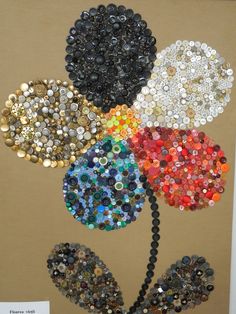 a painting made out of buttons and beads on a brown background, with a flower in the center