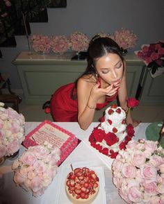 a woman in a red dress sitting at a table with flowers and a wedding cake