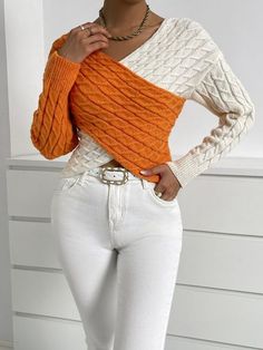 a woman in white jeans and an orange sweater poses for the camera with her hands on her hips