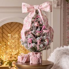 a small christmas tree with pink bows and ornaments on it, sitting on a table in front of a fireplace