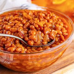 a glass bowl filled with baked beans on top of a wooden table