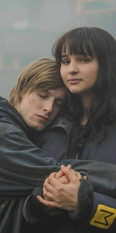 two people are hugging each other in the foggy city street, one is wearing a black jacket and the other has long dark hair