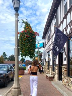 a woman in white pants walking down a street next to a tall lamp post with a sign on it