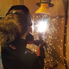 a woman working on a piece of metal in a factory with sparks coming out of it