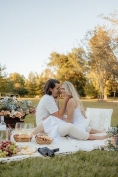 a man and woman sitting on a blanket in the middle of a field with food