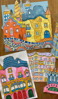 four different colored paper houses on a wooden table next to some scissors and glue stickers