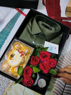 a box filled with red roses sitting on top of a bed next to a woman's hand