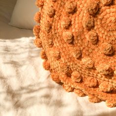 an orange crocheted blanket on top of a bed with white sheets and pillows