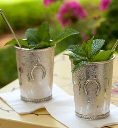 two silver cups filled with mint leaves on top of a table