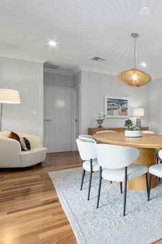 a dining room table with white chairs and a rug on top of the wooden floor