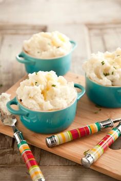 three blue bowls filled with mashed potatoes on top of a wooden cutting board