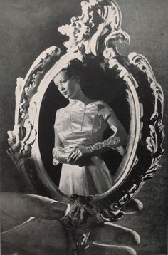 an old photo of a woman standing in front of a mirror with her hands on her hips