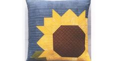 a blue pillow with a sunflower on the front and brown center, sitting on a white surface