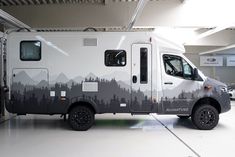 an rv parked in a garage with mountains painted on the side and trees printed on the back