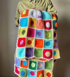 a man holding a multicolored crocheted blanket