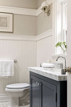 a white toilet sitting next to a sink in a bathroom under a window with framed pictures on the wall