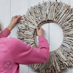 a woman is making a twig wreath out of driftwood and sticks on the wall