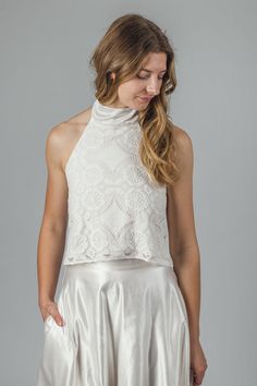 "The 'Aster' halter neck top This halter neck top is handmade in off-white cotton lace, lined in a soft organic cotton jersey. The neck tie is in organic cotton/ silk satin, which has a gentle sheen to it. The ties can be be tied at the back of the neck with a bow or left long. The top closes at the back with little covered buttons and rouleaux loops. This top is individually made to order in sizes XXS - XXL, please refer to size chart below. It can also be made to custom sizes/lengths. For sizing advice or to submit your measurements please get in touch.  It is available to order in off-white/ ivory. The standard length is 18\" from shoulder to hem. Made from 95% cotton, 5% nylon. Lined in 100% organic cotton jersey.  This top is made to order, designed, cut and stitched by me in England. Delicate Lace Cropped Top For Party, Fitted Lace Halter Neck Top, Fitted Halter Neck Lace Top, Elegant Lace Crop Top For Wedding, Elegant Lace Bodice Top For Wedding, Elegant Wedding Tops With Lace Bodice, Spring Lace Top With Lace Back, Delicate Lace Crop Top, Elegant Cropped Lace Top With Scalloped Edges