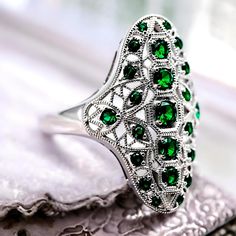 Step into timeless elegance with our Vintage Rhodium Plated 925 Solid Sterling Silver Simulated Emerald Ring. This exquisite piece is expertly crafted, featuring round-cut vibrant green simulated emerald stones that instantly captivate with their radiant hue. The ring is stamped with 925, ensuring its authenticity and superior quality. Each facet of this sterling silver ring is meticulously polished, granting it a luxurious luster that will elevate any ensemble. This striking ring showcases the craftsmanship and attention to detail synonymous with vintage jewelry. The rhodium plating not only enhances its impressive shine but also provides a protective finish, ensuring durability and long-lasting beauty. Ideal for a variety of occasions - from special events to everyday wear - this versati Luxury Jewelry With Polished Round Stone, Luxury Sterling Silver Emerald Ring With Gemstone Accents, Luxury Stamped 925 Emerald Ring As Gift, Luxury Green Emerald Ring Stamped 925, Luxury Stamped 925 Green Emerald Ring, Exquisite Luxury Silver Emerald Ring, Luxury Green Emerald Ring In Sterling Silver, Luxury Faceted Green Rings, Luxury Faceted Round Cut Jewelry