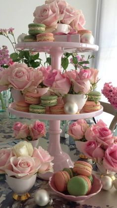 three tiered trays filled with pink roses and macaroons on a table