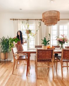 a woman standing in the middle of a dining room table with potted plants on it