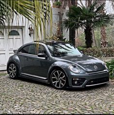 a gray volkswagen beetle parked in front of a house on a cobblestone driveway