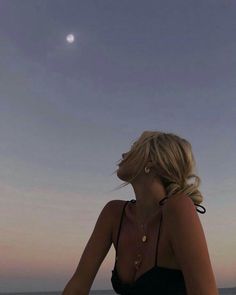 a woman sitting on the beach watching the sun go down