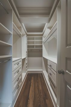 an empty walk - in closet with white cabinets and wood flooring is seen here